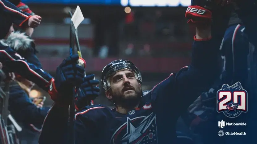 A Columbus Blue Jackets player celebrating, with the 20th anniversary mark
