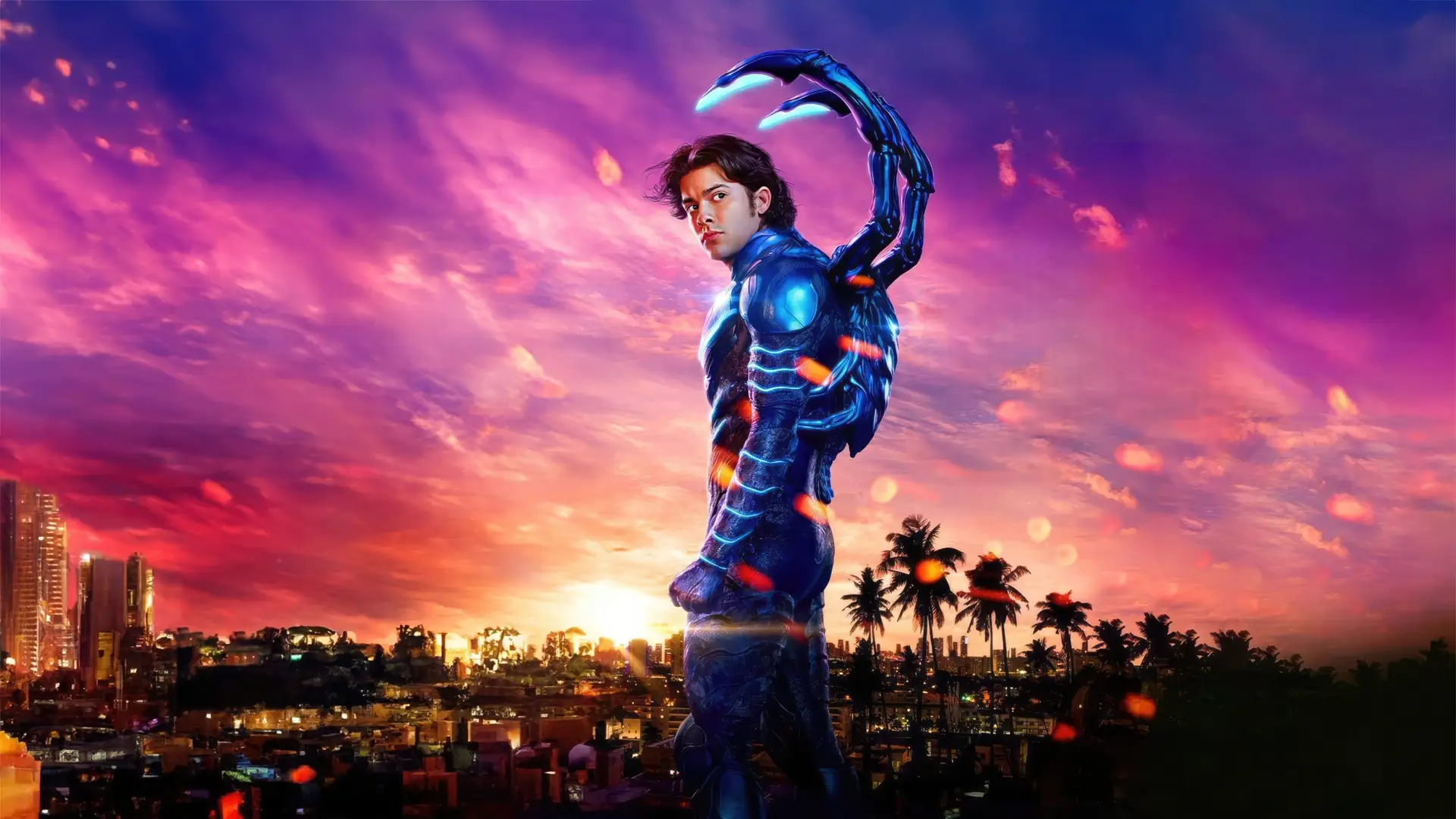 Xolo Maridueña as Blue Beetle, in a blue suit with glowing parts, standing against a sunset city skyline.