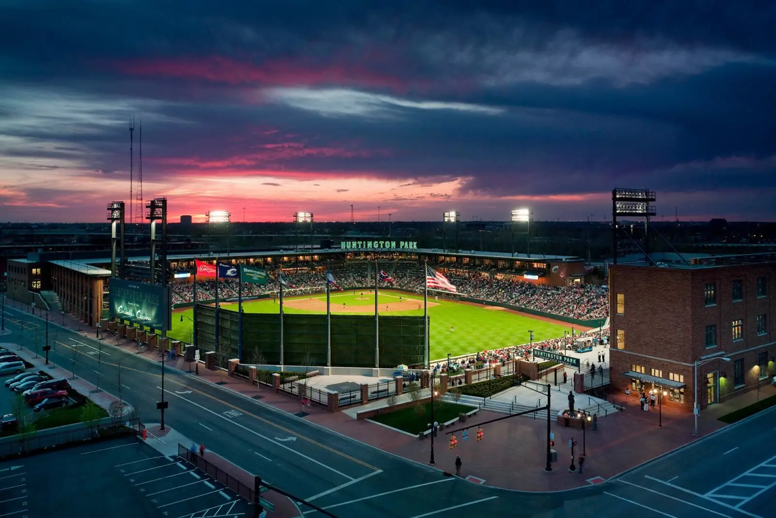 An aerial shot shows Huntington Park lit up at dusk, with a vibrant sunset over the city skyline in the background.