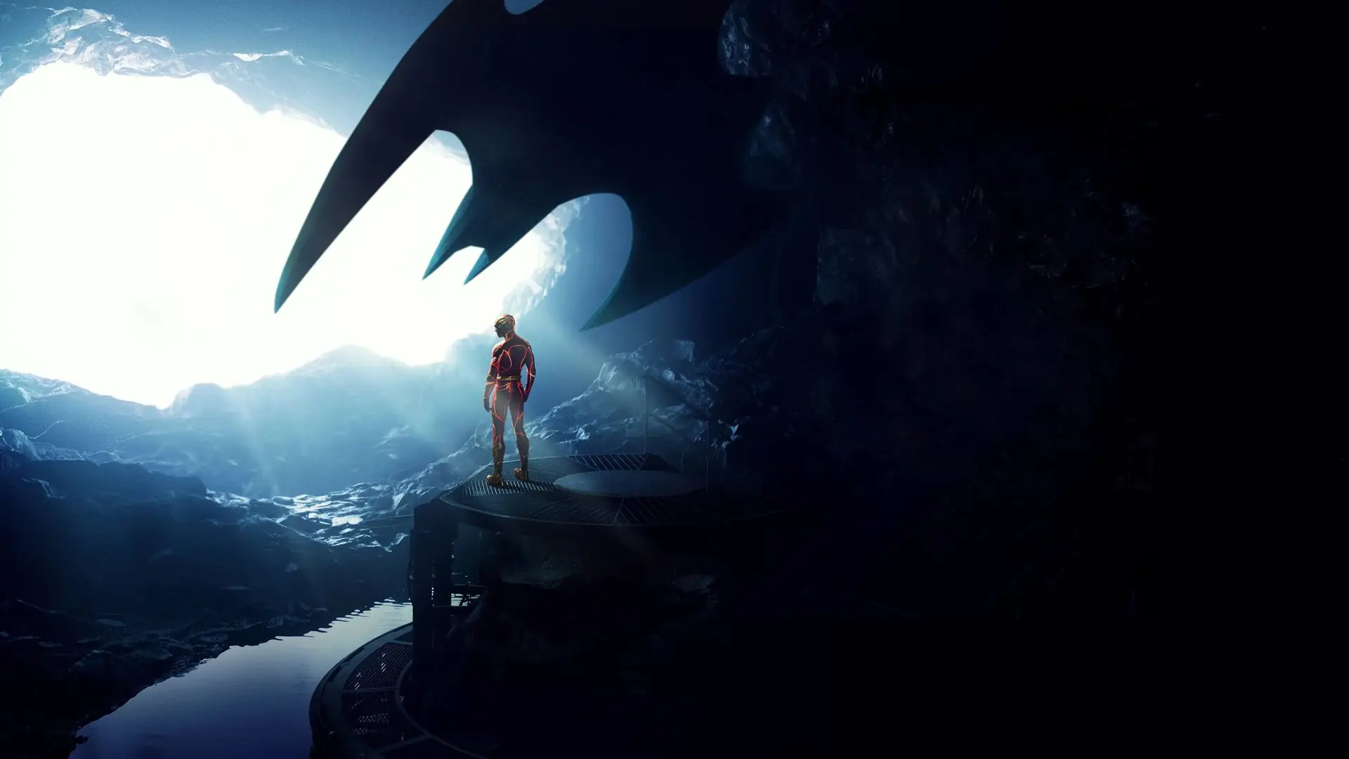 The Flash stands on a circular platform in a dark cave, looking toward a bright opening beneath a large bat symbol.