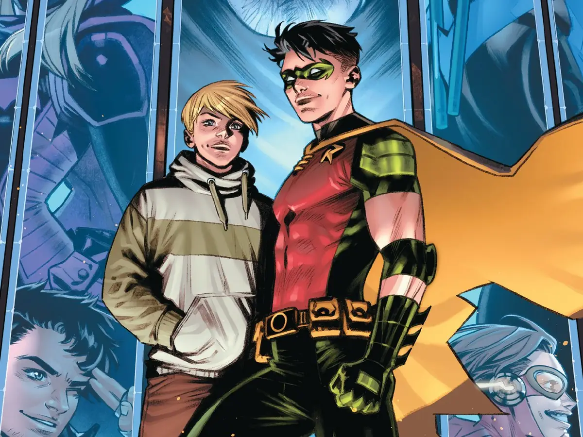Two young men stand side-by-side, one wearing a superhero costume with a red top and yellow cape, and the other in a hoodie.