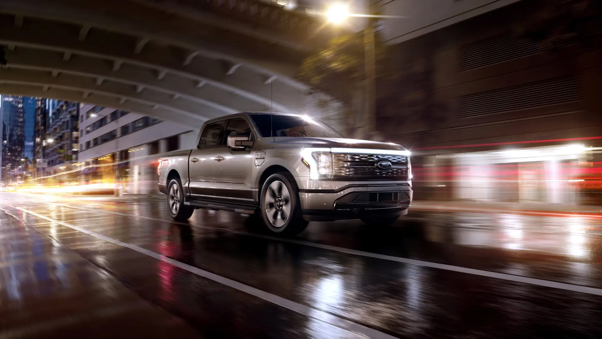 A Ford F-150 Lightning drives under a bridge at night.